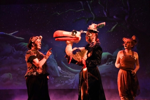 A picture of actors with a bird puppet in front of a projection of the African forest at nighttime