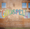 A curtain warmer of a brick building with windows and the Godspell logo in rainbow lettering